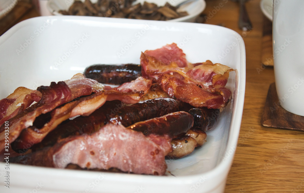 Greasy fried bacon and sausages on a white ceramic plate - typical English breakfast Greasy fried bacon and sausages on a white ceramic plate - typical English breakfast