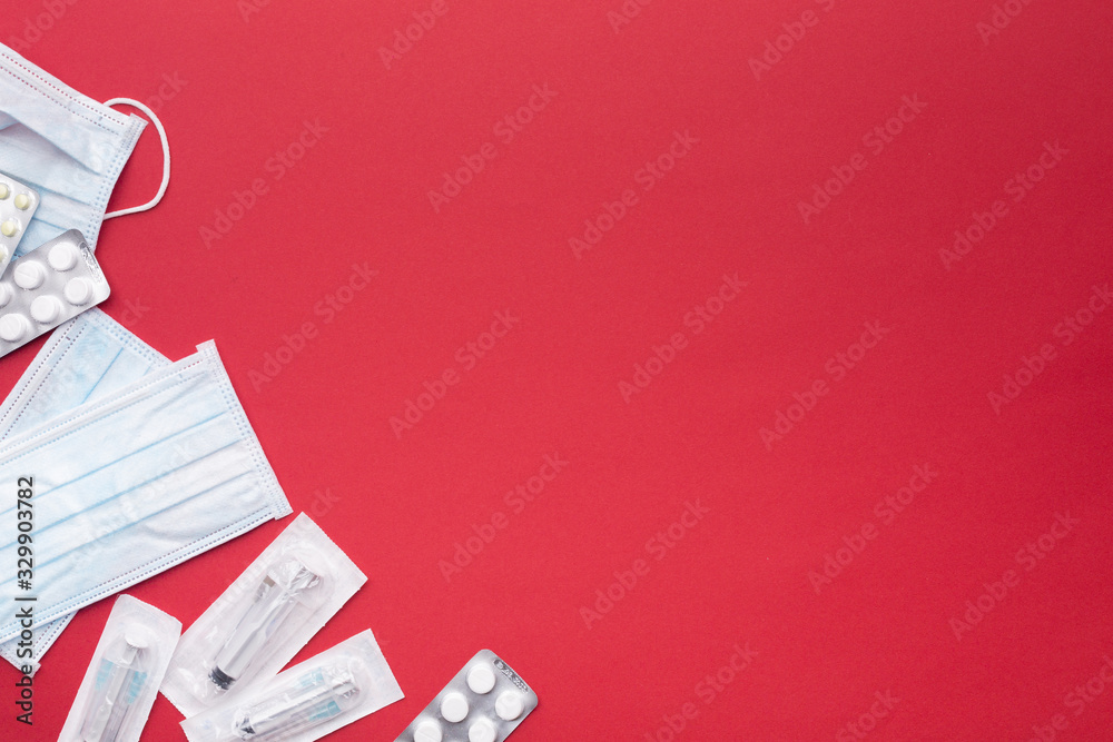 Medical protective masks, disposable syringe in sterile packaging and pharmaceutical packaging with pills on paper, red; bright background. The concept of protecting health from the virus. Copy space