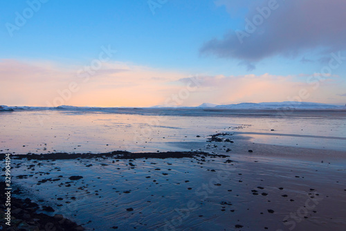 Dark clouds developing in a blue sky with a pink horizon over the coast of Iceland at sunset, with the shoreline in the foreground 
