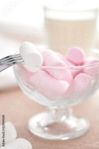 marshmallows in a glass bowl stands on a light table with a fork and milk.