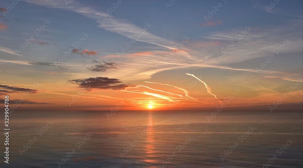 Beautiful golden sunrise over a calm sea with blue sky and stunning clouds Beautiful golden sunrise over a calm sea with blue sky and stunning clouds