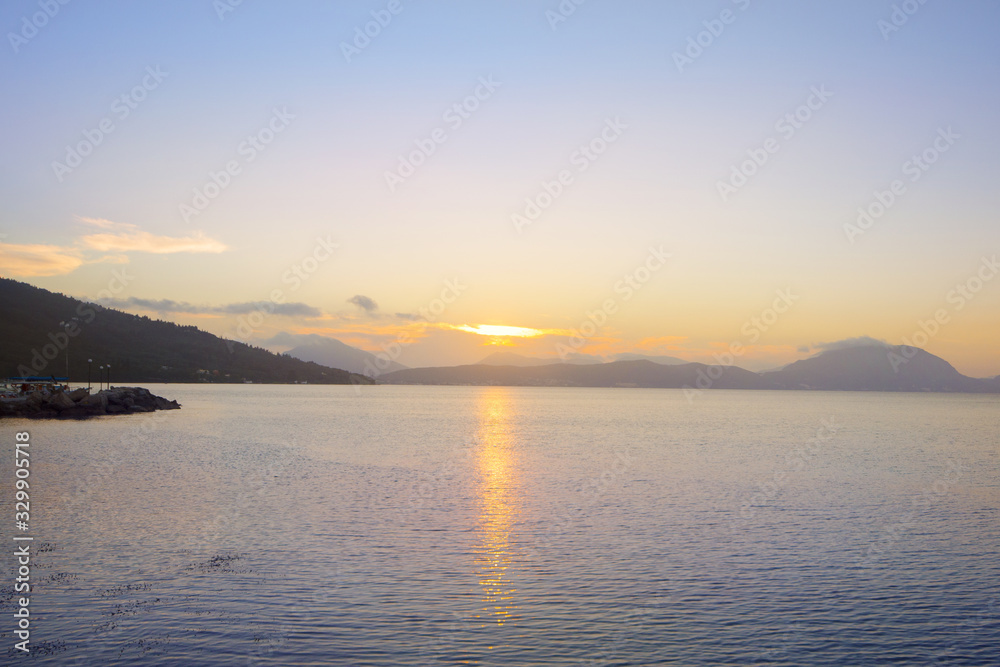 Serene bay on Corfu coast with the sun setting behind distant mountains