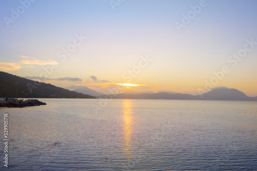 Serene bay on Corfu coast with the sun setting behind distant mountains