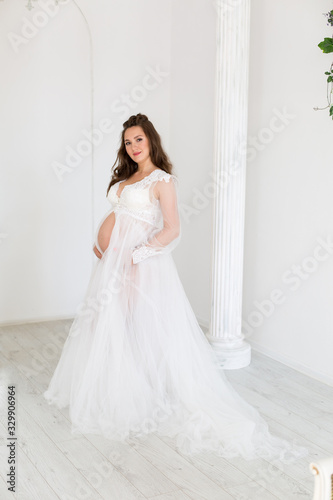 a pregnant girl in a white negligee hugs her stomach with her hands