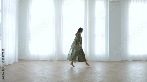 a girl in a long dress walks around the apartment smiling, white curtains