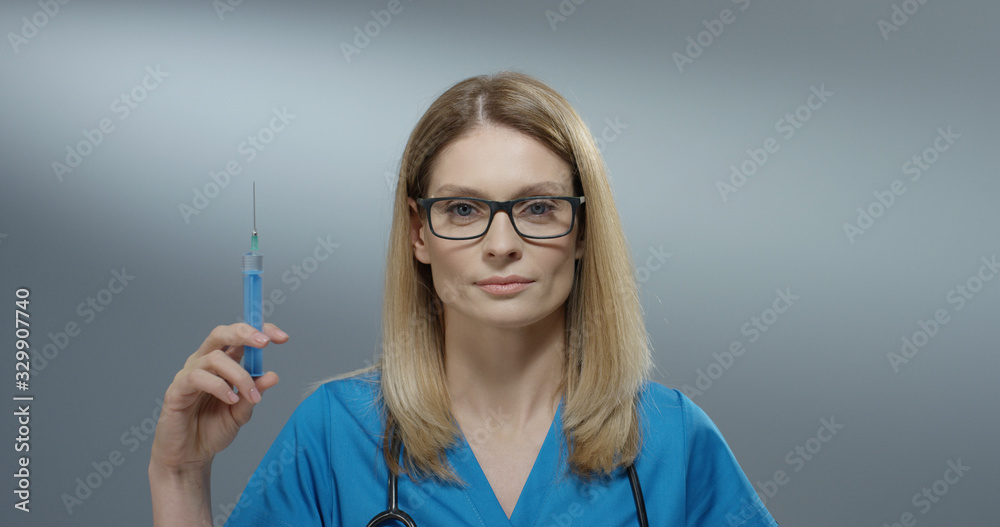 Close up of the Caucasian attractive woman physician in the glasses holding a syringe with a needle and withdrawing fluid.