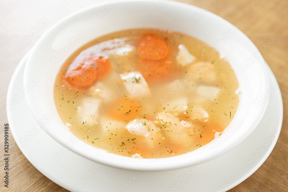 Fish soup in a white plate. Fish soup with vegetables, celery in a cup for the broth. Pike perch and salmon. Plate on wooden table. Restaurant menu