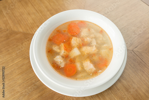 Fish soup in a white plate. Fish soup with vegetables, celery in a cup for the broth. Pike perch and salmon. Plate on wooden table. Restaurant menu