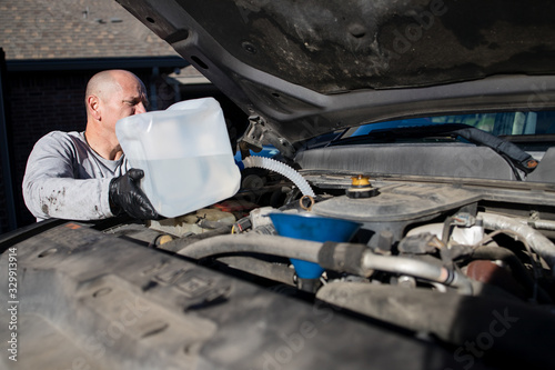 Partial view of man pouring diesel engine fluid into a diesel truck, part of DIY auto maintenance. DEF fluid helps reduce the air pollution caused by diesel engines.
