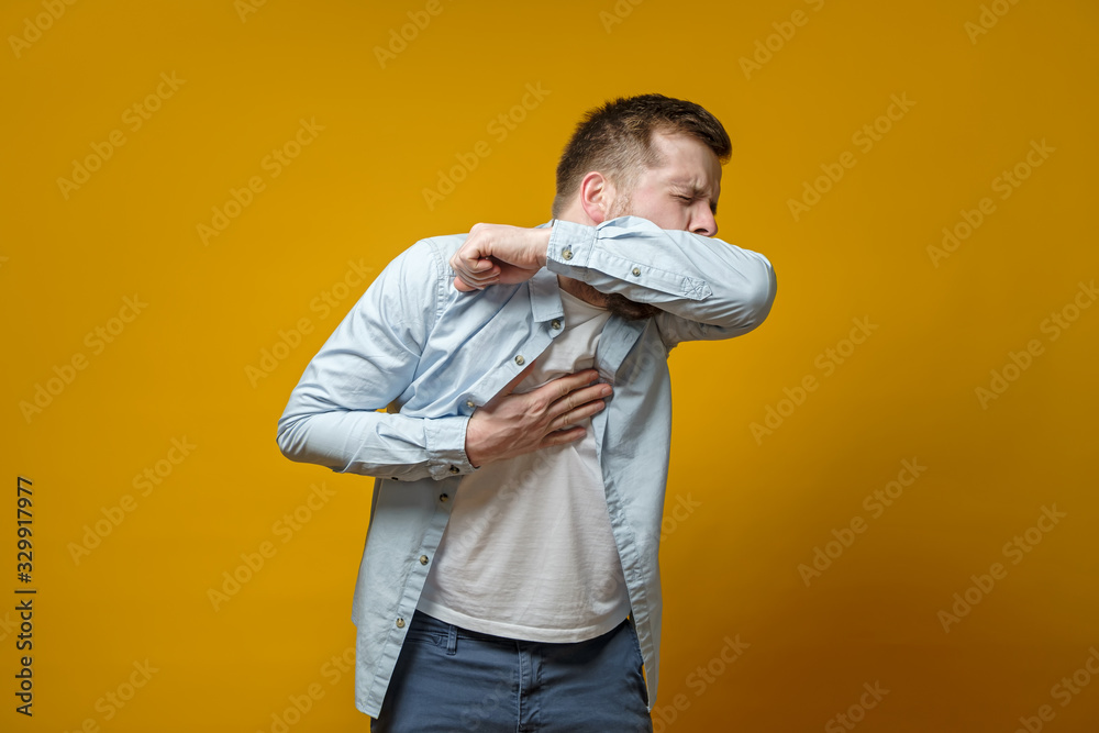Мan coughs in his elbow and holds hand on chest, experiencing pain. Correct sneezing. Concept of