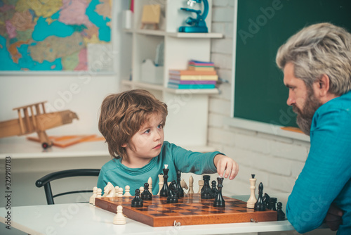 Concentrated little boy - father and son sitting at the table and playing chess. Boy with father teaching and learning chess at home. Child early development.