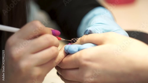 Manicurist draws a pink pattern on a black nail
