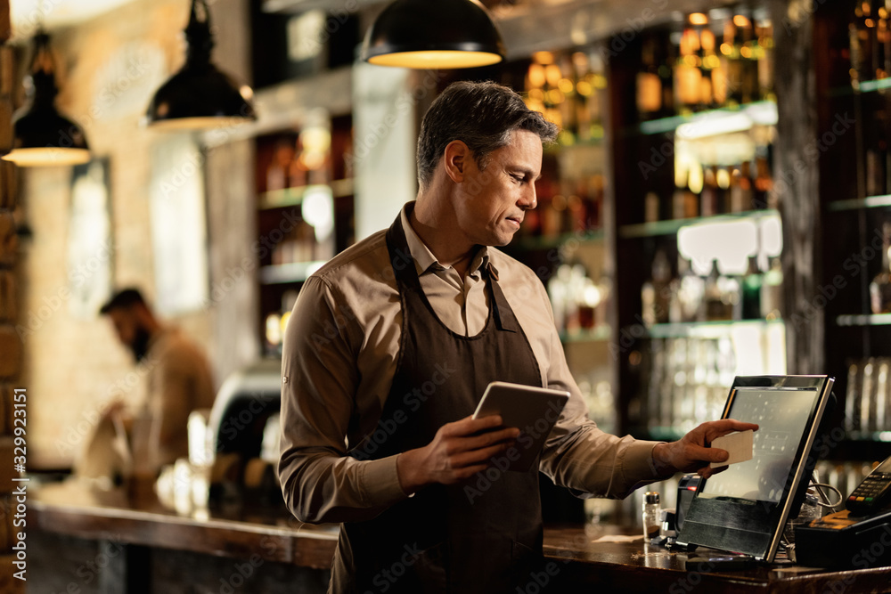 Smiling bartender at cash register working in a pub. Smiling bartender at cash register working in a pub.