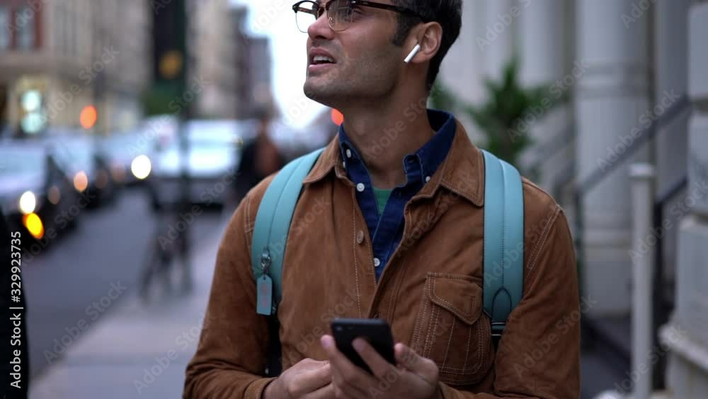 Slow motion effect of Spanish male tourist in spectacles for eyes protection standing outdoors and making mobile international conversation, hipster guy in earphones communicating via app Slow motion effect of Spanish male tourist in spectacles for eyes protection standing outdoors and making mobile international conversation, hipster guy in earphones communicating via app