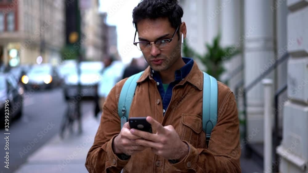 Hispanic male tourist in trendy eyewear and electronic headphones using application on cellphone for communicate in roaming, hipster guy in earphones typing text for sending message via mobile