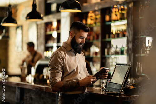 Young bartender using digital tablet while working in a pub. © Drazen