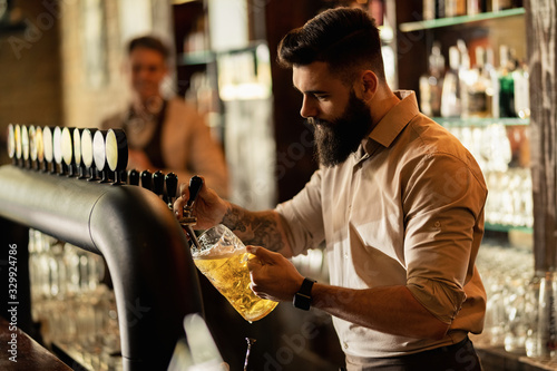 Young bartender pouring draft beer form beer tap in a pub. © Drazen