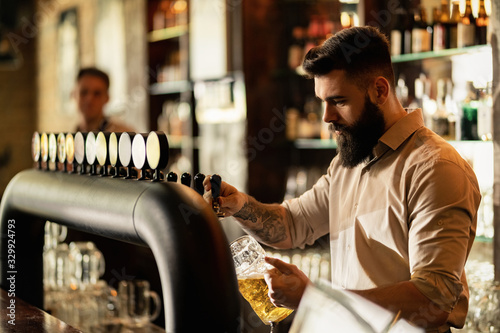 Young bartender pouring beer from beer tap while working in a pub. photo