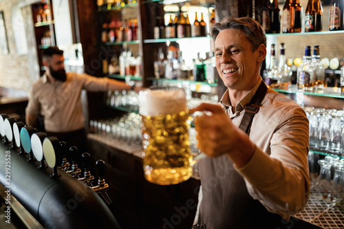 Happy barista holding glass of draft beer in a bar.