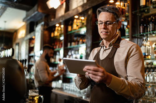 Smiling mid adult waiter using touchpad while working in a bar.