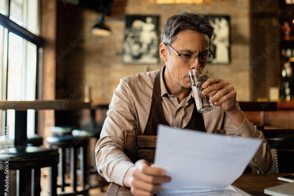 Pub owner drinking water while going through paperwork.
