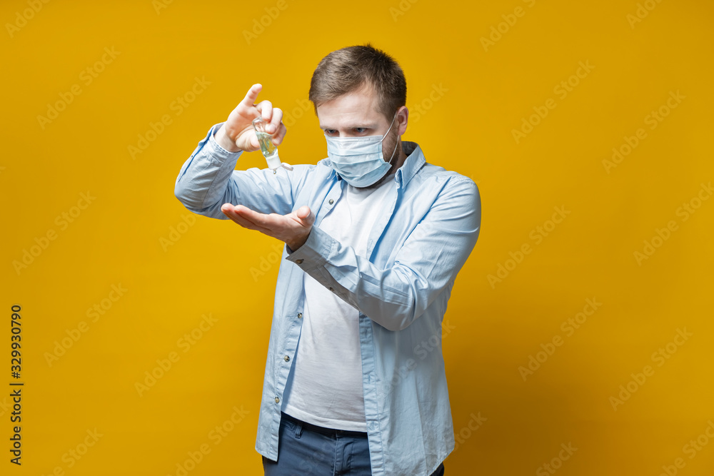 Man in a medical mask gets rid of germs on hands with a disinfectant that pours onto palm. Concept of the spread of the virus.