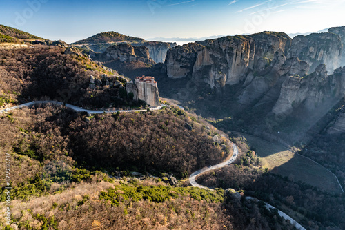 Aerial view of monastery Rousanou and breathtaking picturesque valley and landmark canyon of Meteora at sunset, Kalambaka, Greece, shadows, twisted road, bridge © Vladimir Drozdin