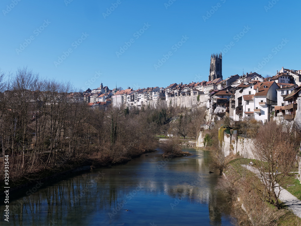 View of the Sarine river and the Auge peninsula in Fribourg, Switzerland. Beautiful houses in the old city and the St-Nicolas cathedral on the right.