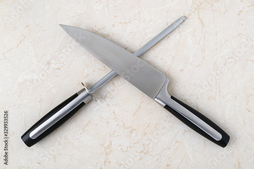 Fotografija Professional chef knife and a sharpening steel lying crosswise on a kitchen table