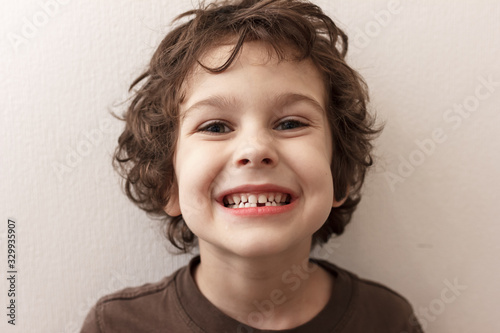Charming curly boy smiles without tooth on white background. The boy lost the first milk tooth. Healthy teeth concept, dental clinic.