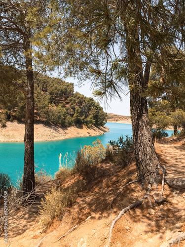 Elevated view through the treetops towards the lake while people enjoy the reservoir in summer. Ardales, Malaga.