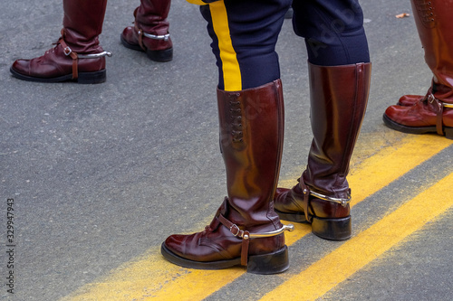 A male police officer stands on a double yellow line in the middle of a paved road, There are two other officers in the background. They are wearing leather boots.