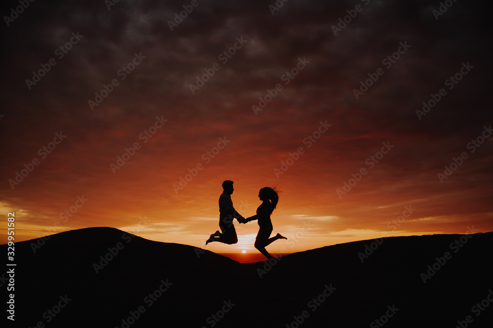 romantic couple in backlight jumping at sunset