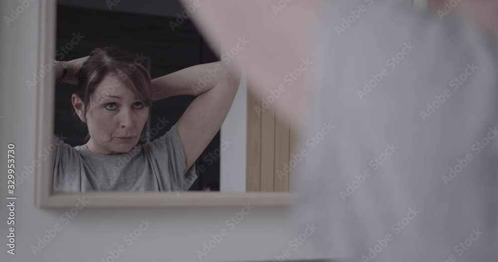 Mature adult female doing up hair in bathroom and looking in mirror Mature adult female doing up hair in bathroom and looking in mirror
