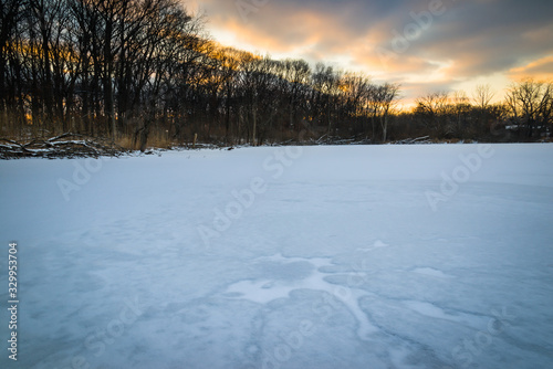 A winter sunset sky over the frozen surface of a woodland lake.