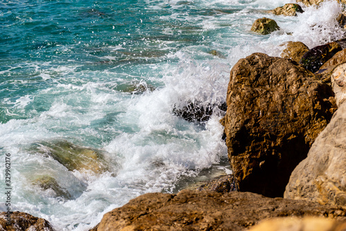 A close-up shot of the Mediterranean Sea turquoise water and powerful waves beating against the rocks on the coast