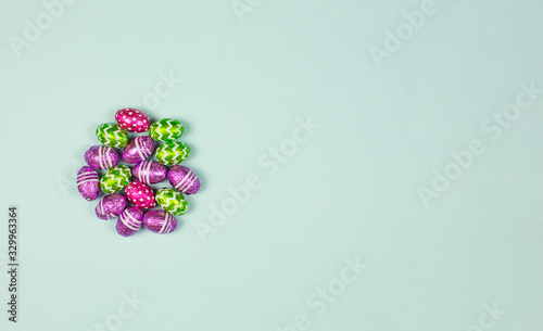 Colorful chocolate easter eggs on blue background. Small Chocolate eggs in a foil. Traditional Easter sweet. Copy Space