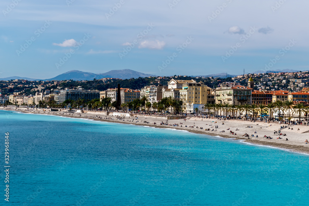 Panoramic wide angle shot of the Quai des États-Unis, people relaxing on the beach of the Mediterranean Sea coastline with the sunlight reflecting in the turquoise water (Nice, France) Panoramic wide angle shot of the Quai des États-Unis, people relaxing on the beach of the Mediterranean Sea coastline with the sunlight reflecting in the turquoise water (Nice, France)