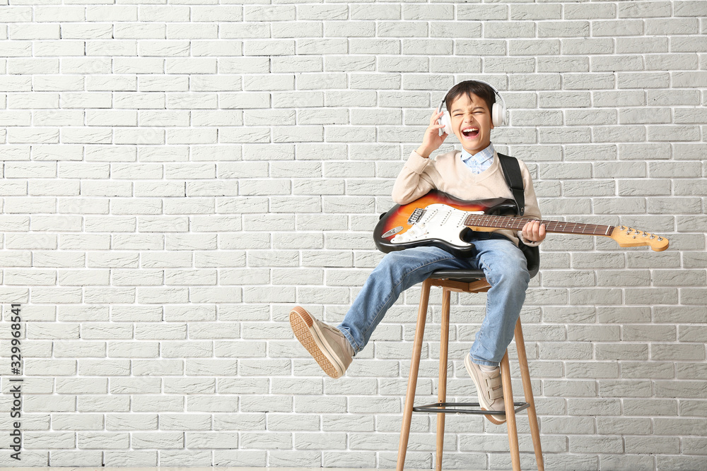 Fototapeta premium Little boy playing guitar against brick wall