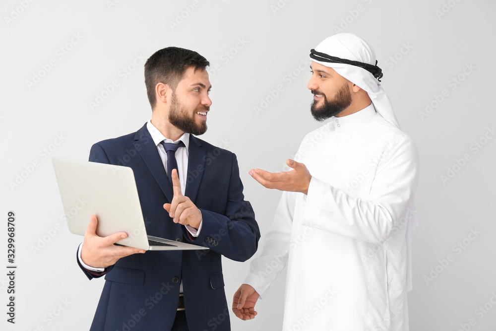 Arab man and his business partner with laptop on grey background Arab man and his business partner with laptop on grey background