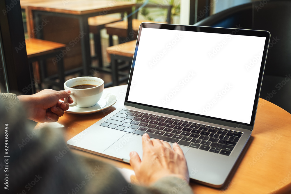 Mockup image of a woman using and touching on laptop computer touchpad with blank white desktop screen while drinking coffee Mockup image of a woman using and touching on laptop computer touchpad with blank white desktop screen while drinking coffee