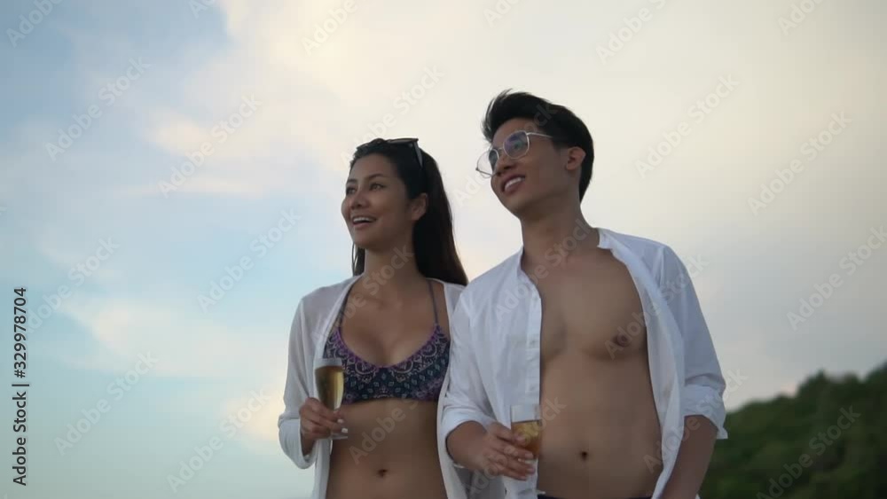 Beautiful young people walking at sunset by the sea, the girl and the boy holding wine glasses and talking nicely to each other slow motion Beautiful young people walking at sunset by the sea, the girl and the boy holding wine glasses and talking nicely to each other slow motion