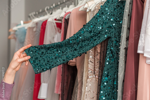 A young woman is choosing a trendy emerald coctail dress with sequins in a fashion boutique.