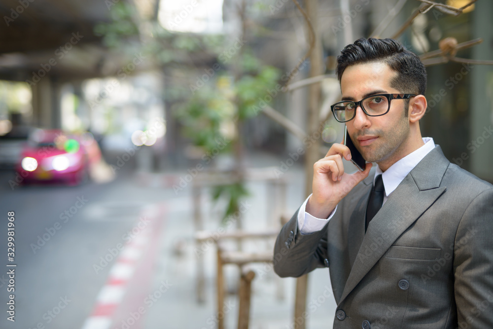 Young handsome Persian businessman talking on the phone in the city streets outdoors Young handsome Persian businessman talking on the phone in the city streets outdoors