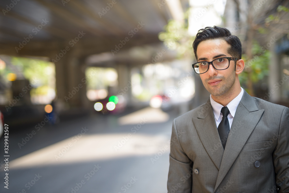 Face of young handsome Persian businessman waiting in the city streets outdoors
