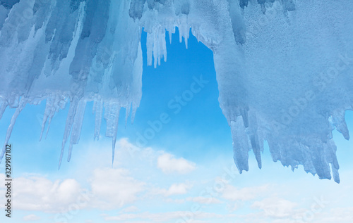 Winter Lake Baikal. View on the blue sky with clouds from an ice grotto in the rocks of Olkhon Island. Ice travel. Blue cold abstract background