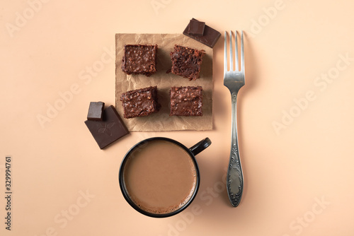 Flatlay with brownie pieces with coffeee cup,chocolate and silver fork on a peach table.