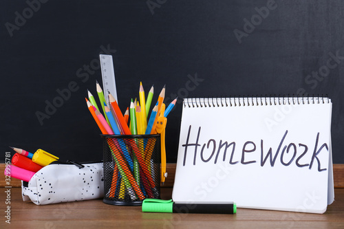 Stationery and notebook with inscription HOMEWORK on wooden table near blackboard photo