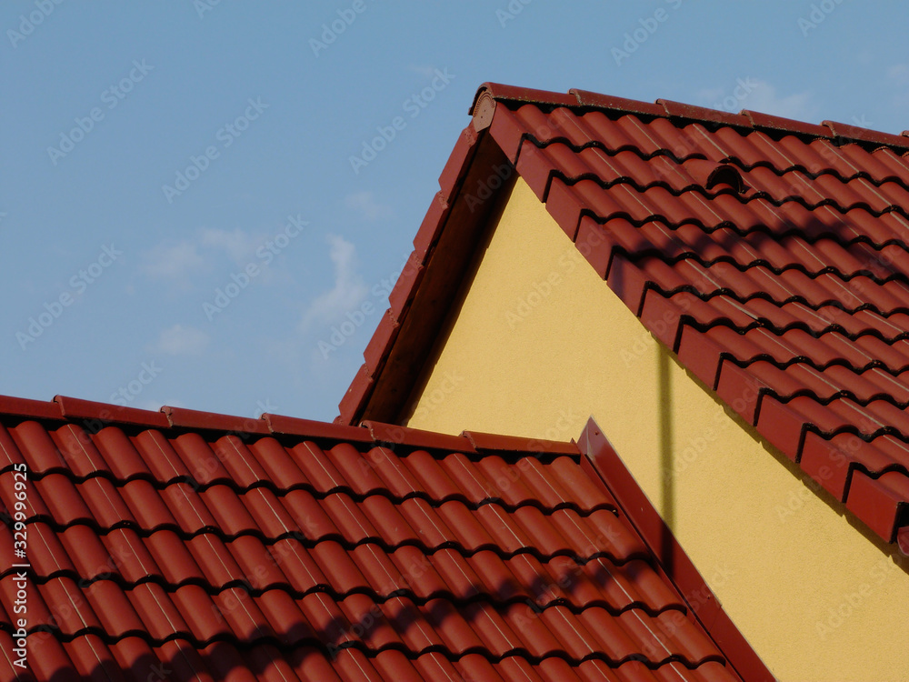 sloped clay roof ridge. red roof tiles and yellow attic fire wall. clear blue sky and white clouds. bright summer sunlight. construction industry and building renovation concept. 