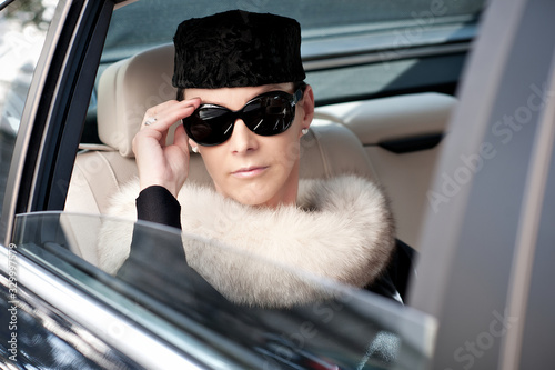 Luxury woman with fur and sunglasses in the back seat of a car